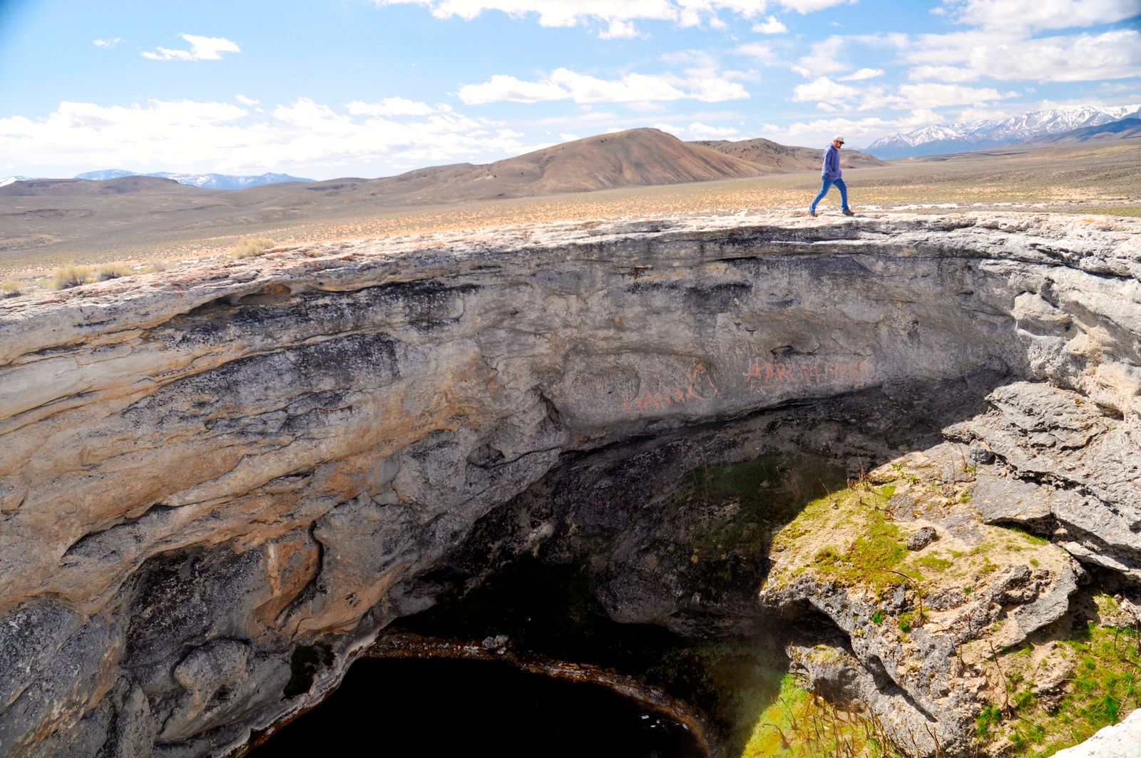 A BLM archaeologist on the rim of Diana's Punch Bowl, with the pool far below