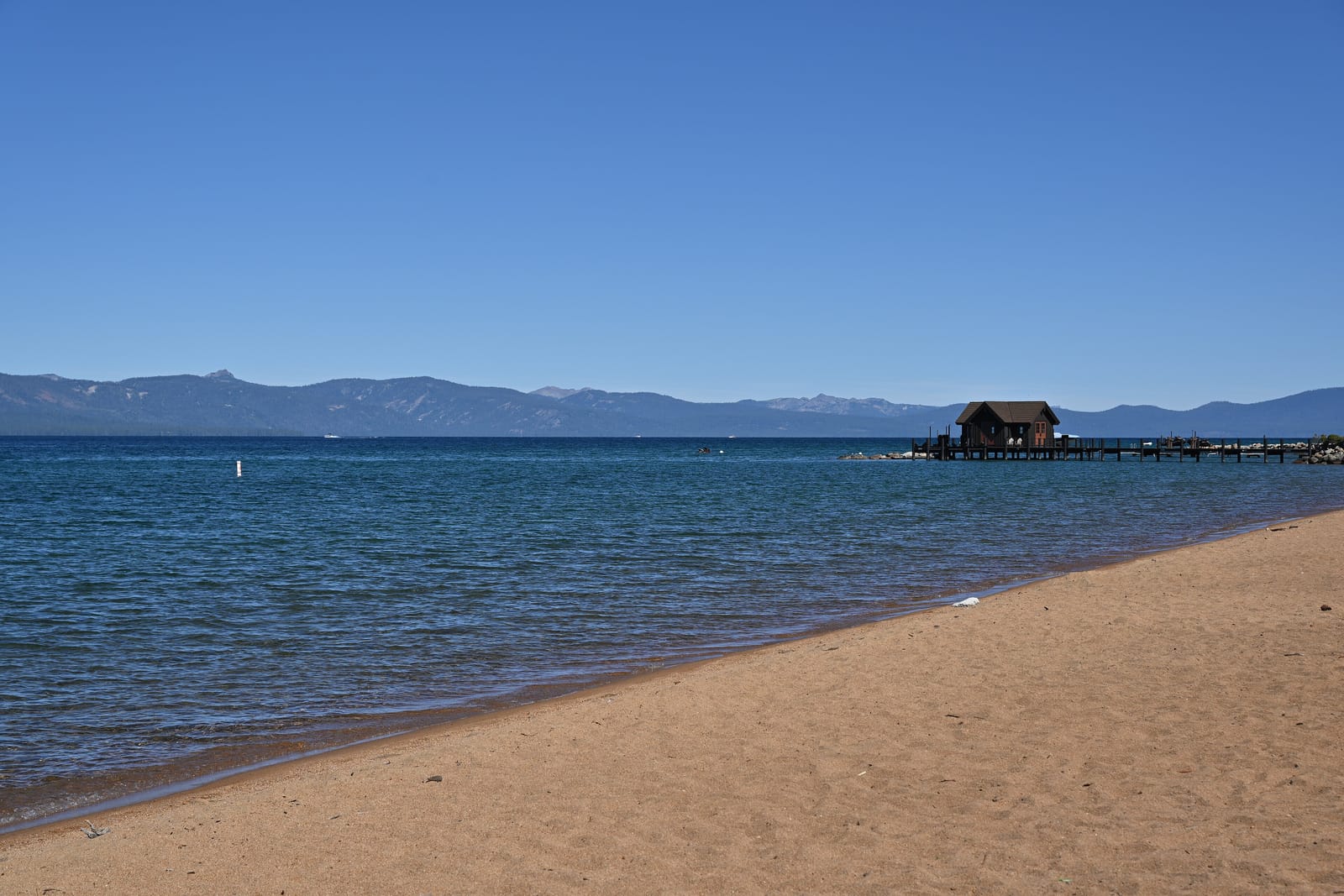 Coarse sand at the water's edge at Nevada Beach, with a pier offshore